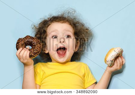 Joyful Child Screams With Happiness. Emotional Girl Eating Tasty Donuts With Chocolate And White Ici