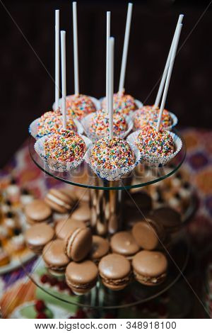 Chocolate Macaroons Lie On A Glass Slide For Desserts. Candy Bar Table. Cakes And Other Sweets.