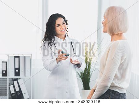 Medicine Concept. Brazilian Doctor Giving Asthma Inhaler To Elderly Woman Whos Sitting On Examinatio