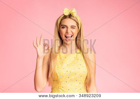 Im Fine. Smiling Blonde Woman Showing Ok Sign, Winking And Looking At Camera Isolated Over Pink Wall