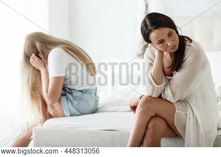 Family conflict and relations concept. Mother and daughter having quarrel and aguring at home. Sad woman and teenage girl sitting on bed. Not looking at each other.