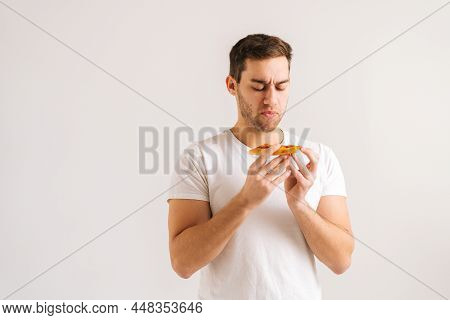 Portrait Of Disappointed Upset Young Man Holding Piece Of Pizza With Awful Smell, Smelling Tainted U