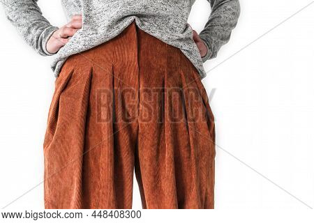 A White Woman Stands In Front With Her Hands On Her Waist, Dressed In A Jumper And Terracotta Trouse