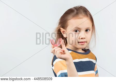 Cute Little Caucasian Girl With Blond Hair Is Holding A Pink Dental Myofunctional Trainer On White T