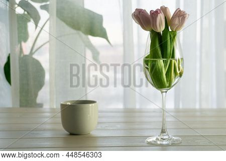 Bouquet Of Pink Tulips In Glass Vase And Cup Of Coffee On Wooden Table Near The Window