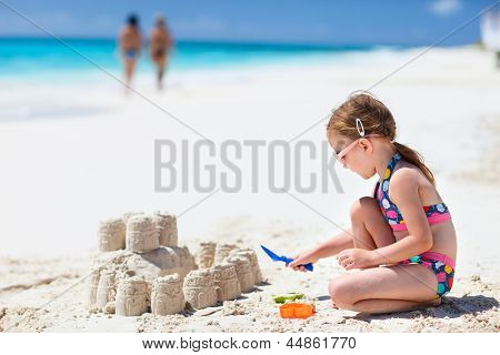Kleines Mädchen am tropischen Strand machen Sandburg