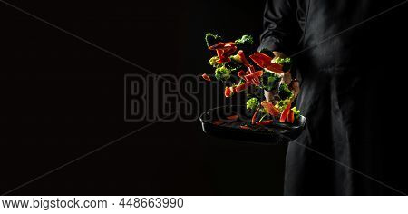Professional Chef Cooks Flambe Style. Hands Of Cook Frying Vegetables On Pan. Flying Vegetables Scat