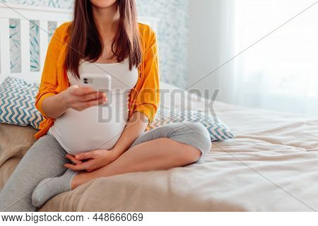 Pregnant Woman With Mobile Phone In Bed. Pregnant Woman Counting Contractions.