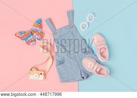 Stylish Summer Set Of Child Clothes. Denim Jumpsuit, Pink Sneakers And Accessories On A Pink Blue Ba