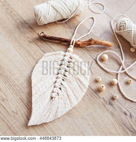Macrame Leaf  In Natural Color And Thread Windings Lying On A Wooden Table. Cotton Rope Decor Macram