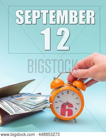 September 12th. Hand Holding An Orange Alarm Clock, A Wallet With Cash And A Calendar Date. Day 12 O