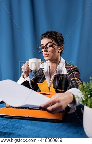 Vintage Style Newswoman With Coffee Cup Holding Empty Paper Near Typewriter On Blue Background