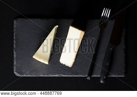 Two Pieces Of Cheesecake Cake On A Slate Black Board With A Serving Fork And Knife On A Black Table 