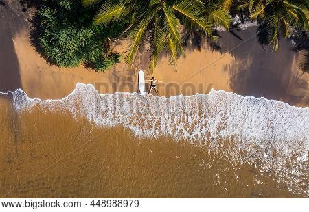 Aerial Photo Of Surfer Lying Next To Surfboard On The Sandy Ocean Shore In Star Pose And Sun Tanning