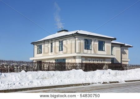 Two-storey cottage and smoke comes out from pipe at frosty and sunny winter day.