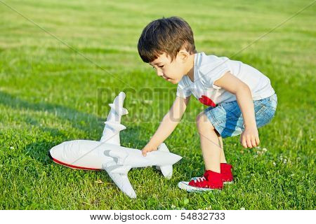 Little boy plays with inflatable model of airplane on grassy meadow