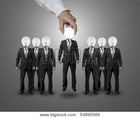 Hand Grab and lift one businessman with lighting bulb head standing with group
