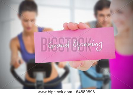 Fit blonde holding card saying grand opening against fitness class in gym