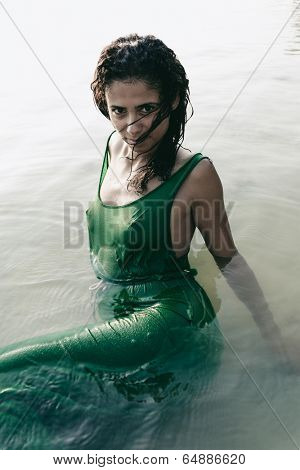 Beautiful sultry woman in a wet clinging dress enhancing her figure standing waist deep in the sea looking up seductively at the camera