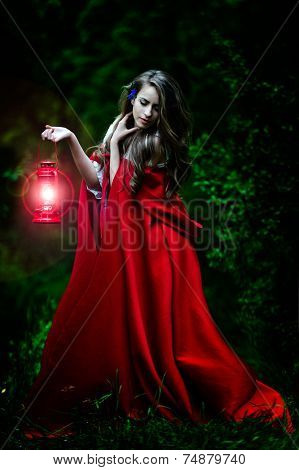 beautiful woman with red cloak and lantern in the woods by night