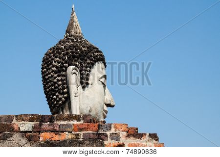 Buddha head behind the wall with clear blue sky