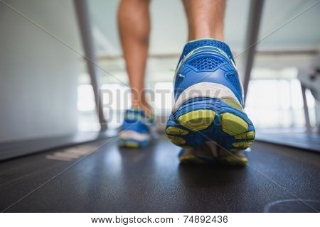 Rear view low section of a man running on treadmill in the gym
