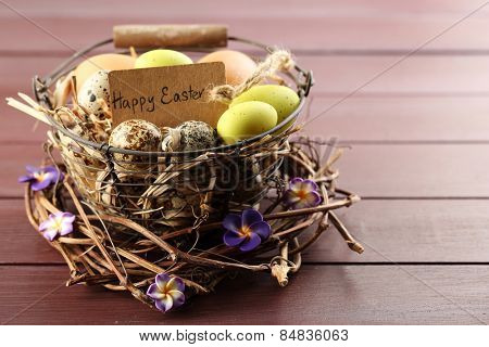 Bird eggs in wicker basket with decorative flowers on color wooden background