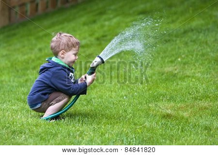 Handsome young boy watering garden with rubber hosepipe