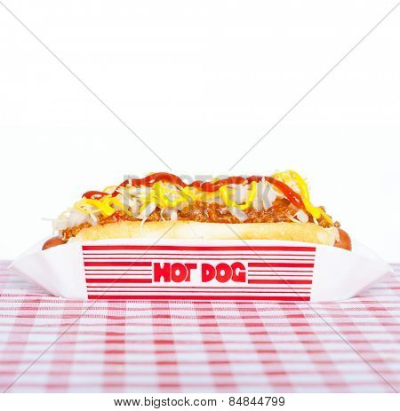 Hot dog with chili, raw onion and sauces on a tablecloth