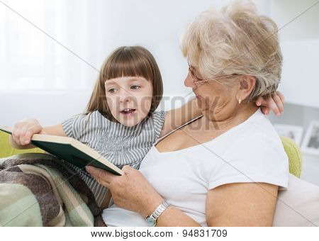 Grandmother is reading a book to her granddaughter