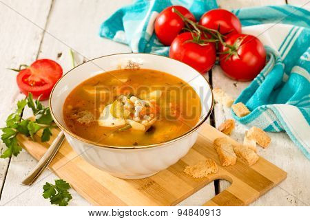 Solyanka, meat and pickle soup on in a white ceramic bowl on a white wooden background.