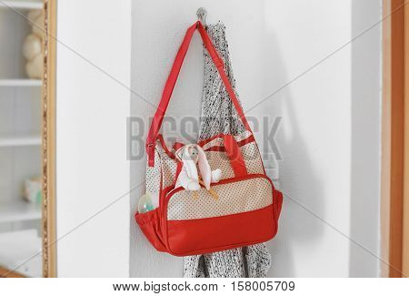 Mothers bag with toy and accessories hanging on wall hook