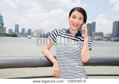 Happy young woman using mobile phone while leaning on railing against cityscape