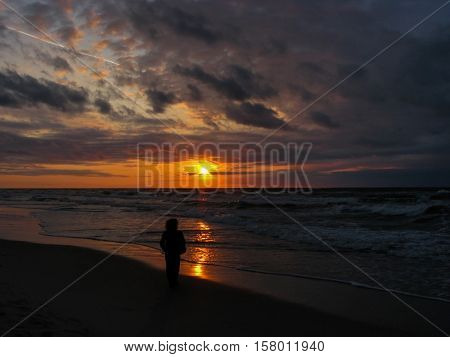 Lonely woman with curly hair is walking along the stormy sea coast towards the sunset