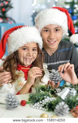 Portrair of smiling brother and sister in Santa hats preparing for Christmas making hand-made decorations