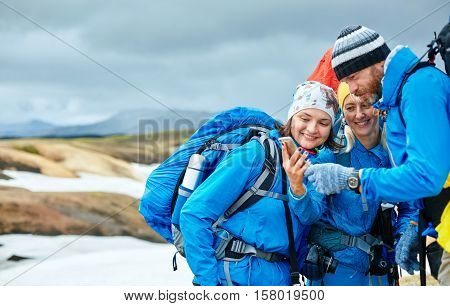couple friends hikers un the Islandic mountains. two woman and one man photographer taking picture on the rhyolite mountains background in Iceland. people looking at the smartphone and laughs