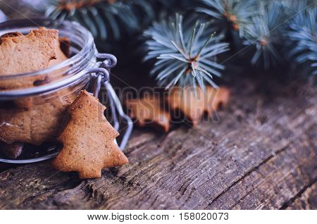 Christmas homemade gingerbread cookies in form of Christmas tree on old wooden table with fir tree. Christmas moody style background. Shallow depth of field. Selective focus. Copy space. Toned image.