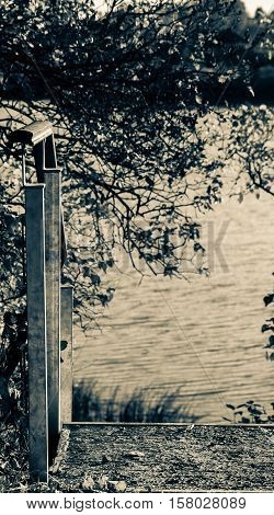 autumn nature, lake landscape with a small staircase leading to the water in the foreground trees, sunny evening, ribbed by waves of pond water, processed, photo in retro style