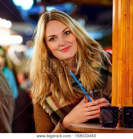 Beautiful young woman drinking hot punch, mulled wine on German Christmas market. Happy girl in winter clothes with lights on background. Family, tradition, holiday concept