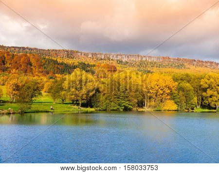 Sandstone rock formation in the middle of colorful autumn forest. Water surface on the foreground. Dramatic evening view. Tisa Rocks, aka Tiske Walls, Czech-Saxon Switzerland, Czech Republic