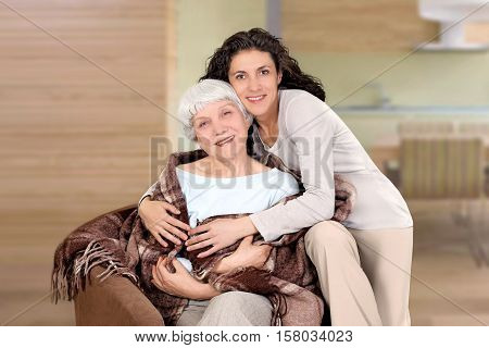 elderly woman and her daughter sitting in a chair with a blanket hug mother grandmother