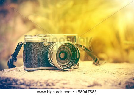 Vintage-style digital camera on boulder on blurred nature background outdoor at the daytime with bright sunlight. Shallow depth of field with focus on camera. Warm tone and vintage effect style.
