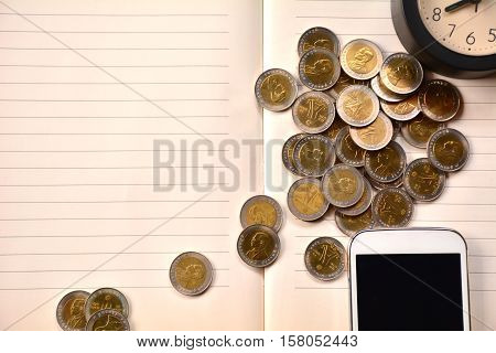 Coins, smart phone and clock put on notebook.