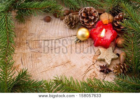 Christmas decoration with red Advent candle and fir branch frame, top view with copy space on wood. Christmas ornaments border with fir tree branches and decoration.