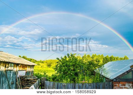 Rainbow in the storm sky with roofs of Russian farm