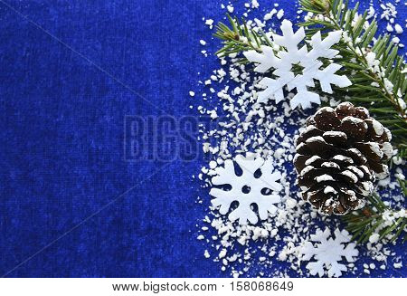Christmas decoration.Decorative felt snowflakes,pine cone and snowy fir tree branch on blue background with copyspace.Winter holidays,Merry Christmas or Happy New Year concept.Selective focus.