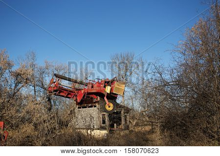 Vintage harvest swather equipment parked on top of an old wooden shed surrounded by forest of bare trees