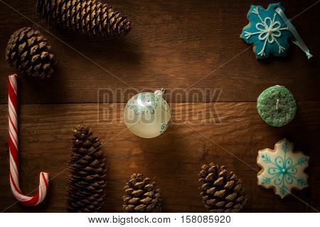 Beautiful christmas frame decoration from peppermint candy cane stick christmas ball candle showflake shaped and patterned bisquit cookies fir cones and pinecones at brown wooden background.