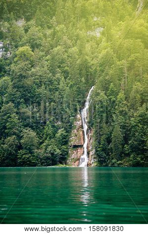 Tall forest waterfall into lake with its reflections at lake of Konigsee in Bavaria Germany