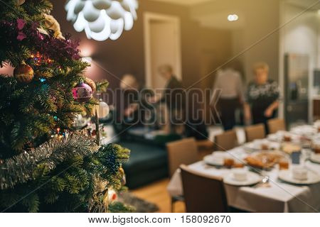 Closeup of decorations hanging from the branches of a Christmas tree in a home with people in the background